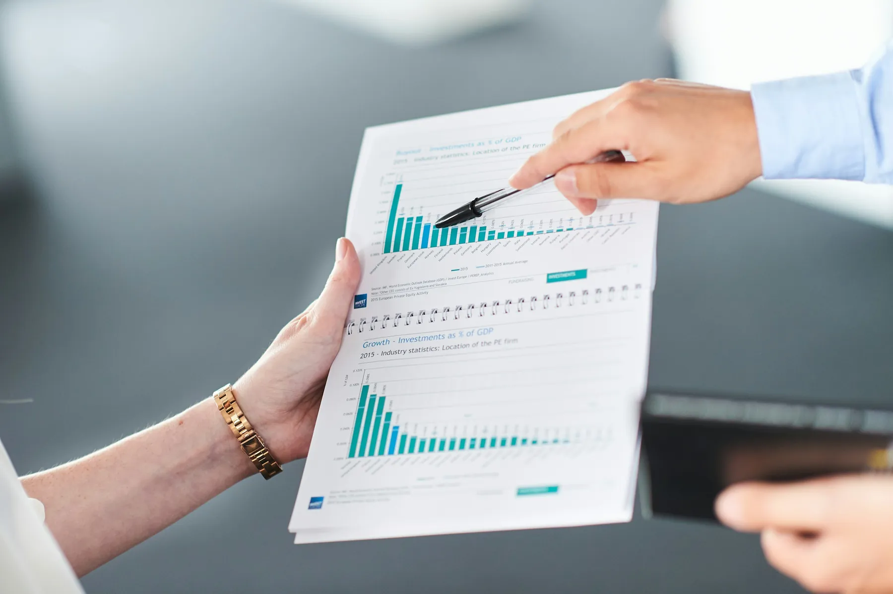 Dos personas analizan con un bolígrafo un informe de inversión impreso con gráficos